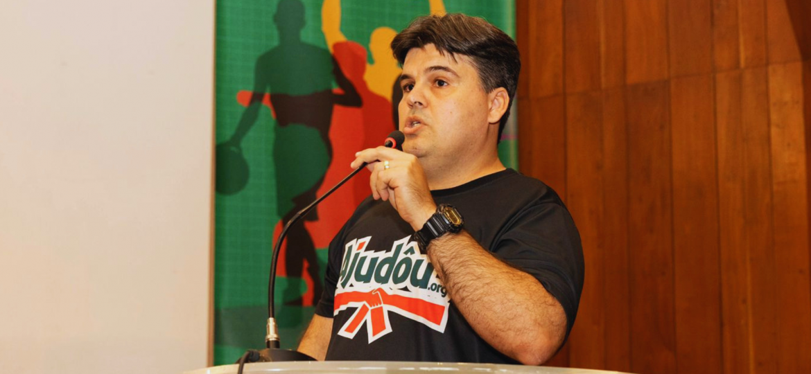 Gestor técnico do Ajudôu durante momento de fala institucional, destacando a importância da liderança, da gestão de pessoas e da organização técnica para a execução qualificada de projetos esportivos sociais. Sua atuação representa a integração entre planejamento, metodologia, acompanhamento de equipes e compromisso com o impacto social por meio do esporte.