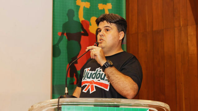 Gestor técnico do Ajudôu durante momento de fala institucional, destacando a importância da liderança, da gestão de pessoas e da organização técnica para a execução qualificada de projetos esportivos sociais. Sua atuação representa a integração entre planejamento, metodologia, acompanhamento de equipes e compromisso com o impacto social por meio do esporte.